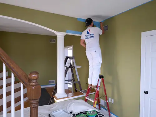 Painter brushing a ceiling edge above a taped staircase